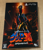 PS5 game case for GUP-X Special Pack, featuring a dynamic robot illustration in red, blue, and yellow against a fiery orange and black background, photographed on a light wood surface.