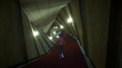 A person in a pink top and blue jeans walks down a long, narrow corridor with a red carpet and warm wall lights.