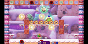 A screenshot from a colorful video game scene with a whimsical candy-themed environment, floating gold orbs, a character near the bottom center, and a UI bar at the bottom showing score and icons.