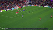 Soccer match in progress with players on a field, surrounded by spectators and advertisements.