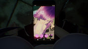 A black smartphone held in a dark environment, displaying a pink anime wallpaper with a purple-haired character. The phone is centered, with blurred dark shapes in the foreground and background.
