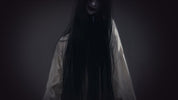 Person wearing a long black hooded garment against a dark background