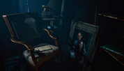 Dark room with a chair, table, and framed picture of a man holding a gun.