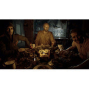 A dark, low-lit scene showing three people seated around a table in a dim interior, with a skull and candles on the tabletop.