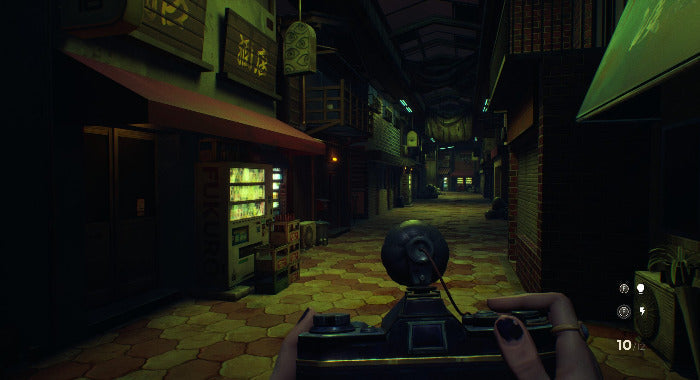 A first-person perspective in a dark, narrow alleyway with storefronts on both sides, viewed from behind a character holding a black device. The scene is dimly lit with warm yellow and orange tones from the floor and shop lights, with Japanese signage visible on the buildings.