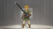 A collectible action figure of Link from The Legend of Zelda, standing on a light-colored platform in a misty gray environment. The figure is wearing his signature green tunic, white trousers, and brown boots, and holds a large sword over his shoulder.